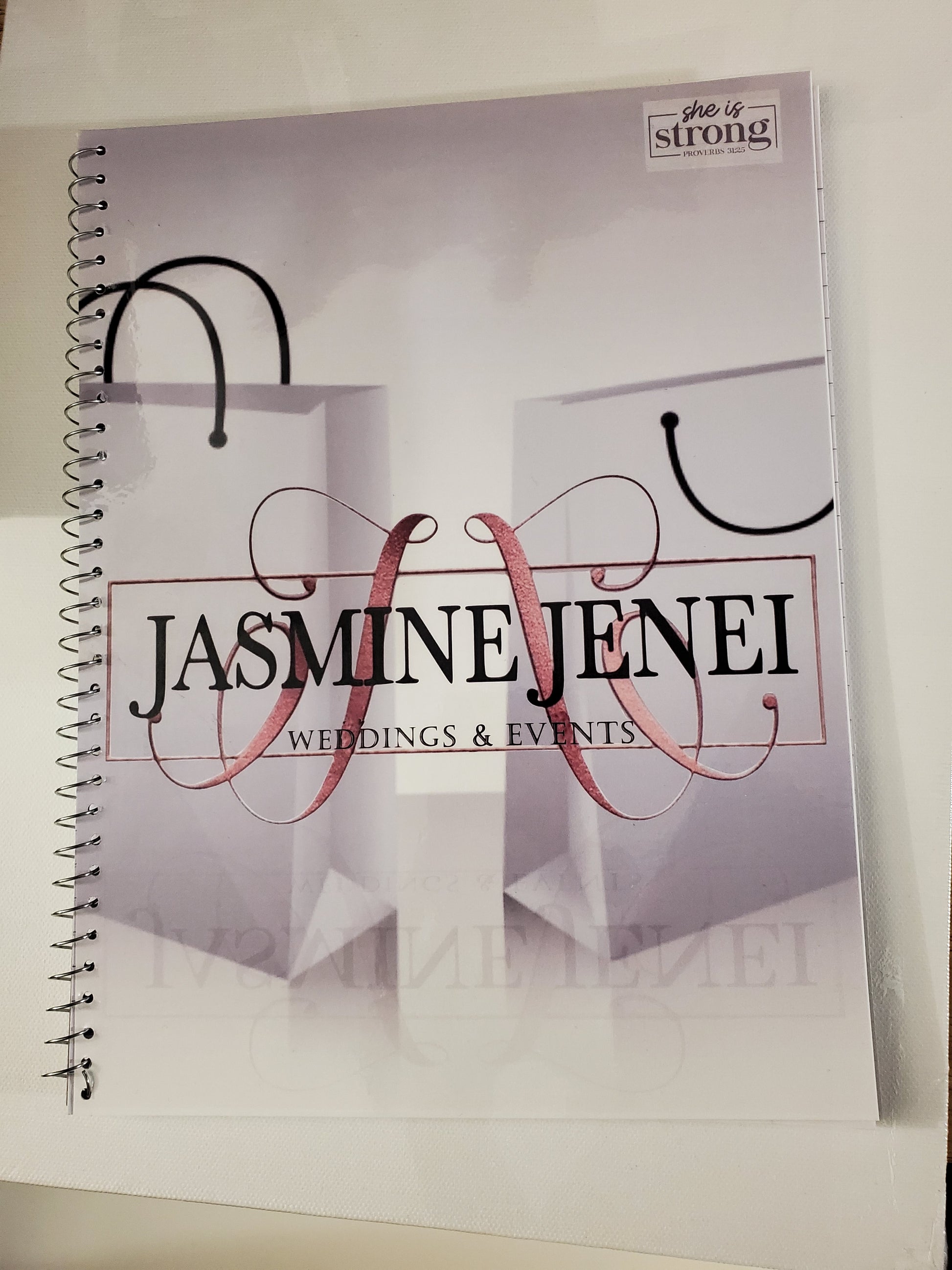 A spiral Notebook with the Business name in Fancy font that reads "Jasmine Jenei Wedding & Events"